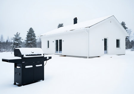 Barbecue grill covered in snow outside a modern white houseの素材