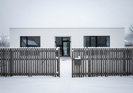 Modern white house facade seen through an open wooden fence in snowの素材