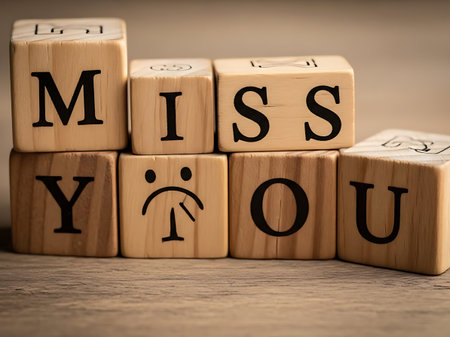 Wooden block spelling out miss you with sad face iconの素材