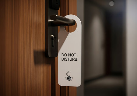Close up of a white do not disturb sign hanging on a wooden hotel room door handleの素材