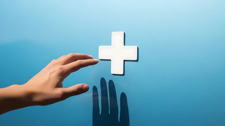 Hand reaching out to touch a floating white plus sign symbol against blueの素材