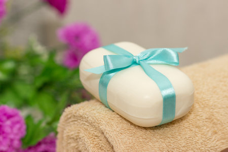 Soap with blue ribbin bow on towel and witn purple flowers on the background