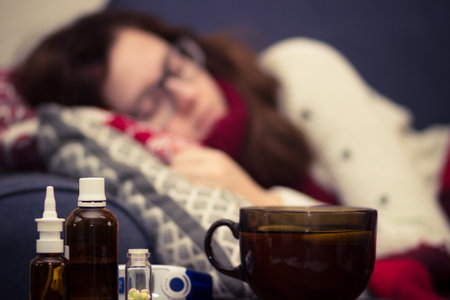 Sick woman in a scarf sleeping on the bed next to pills and drugsの写真素材