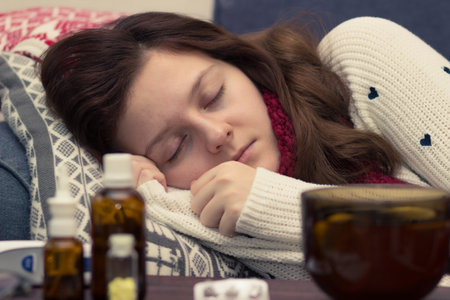 Sick woman in a scarf sleeping on the bed next to pills and drugsの写真素材
