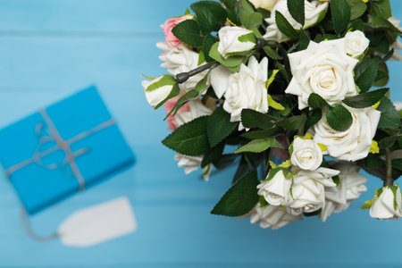 white blank card with a bouquet of roses and blue gitf on a wooden blue background of boardsの写真素材