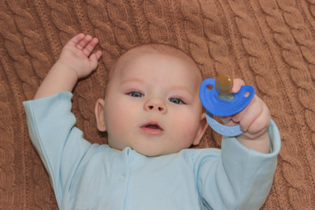 4 month child boy lying happy holding baby nipple soother in hand on a brown background