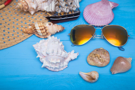 Summer hat, sea shells, colorful sunglasses and toy ship on bright blue wooden backgroundの写真素材