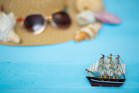 Toy ship, blurred hat, sunglasses and shells on back, on blue backgroundの写真素材