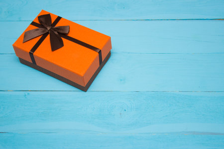orange gift box with brown bow on a blue wooden backgroundの写真素材
