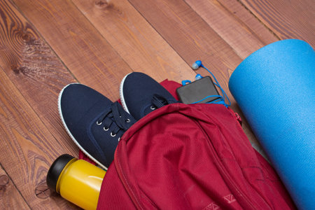 Sports bag with sports equipment: shoes, bottle, smart phone fitness mat on wooden floorの写真素材