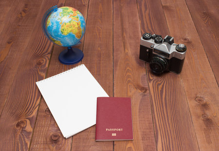 Travel concept - empty notepad, retro camera, globe and passport on brown wooden background. Prepare for journey. Copy space for your text.の写真素材