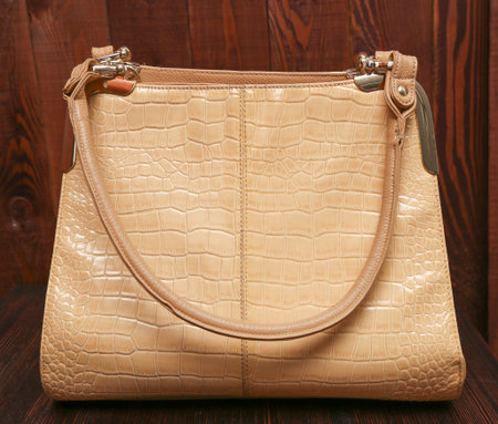 new stylish women's beige leather handbag. Glossy bag on the wooden background