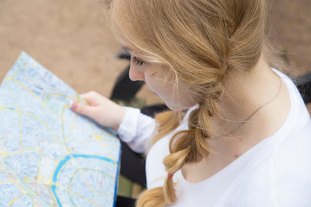 Cute blonde woman in black jeans and hat looking at map, while siting on bench in the forest