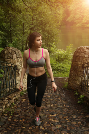 young fitness woman running at forest bridge in the evening, lake at the backgroundの写真素材