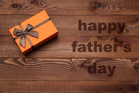 Orange gift box with brown ribbon on wooden background. Happy Fathers Day message.の写真素材