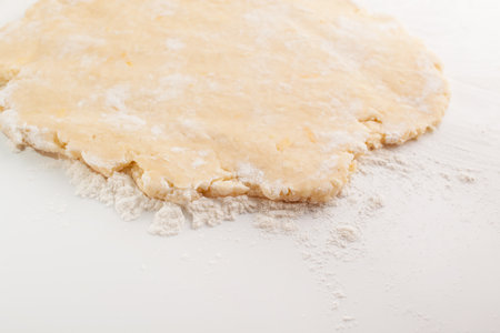 Block of freshly made pastry rolled out on a floured work surface with a wooden rolling pinの写真素材
