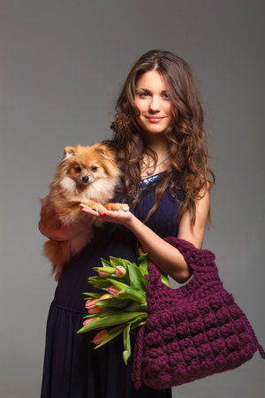 Pretty young woman with long hair holds in hands knitted bag with tulips and spitz dogの写真素材