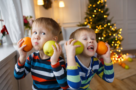 Two little smiling kids, boys drink fruit juice on Christmas tree background. Happy friendly children. Selective focusの写真素材