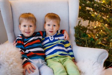 Two little smiling kids, twins boys sitting near Christmas tree. Happy friendly children.の写真素材