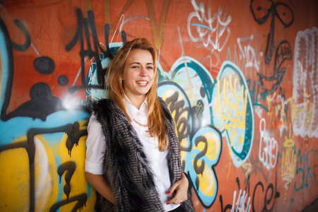 Russian beautiful smiling teenager girl with long blond hair and make up near the wall with graffiti, selective focusの写真素材