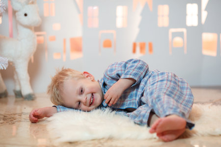 Cute blonde hair little boy in sleepwear near christmas toy paper housesの写真素材