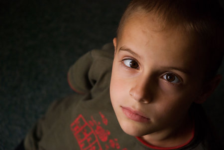 Portrait of a preteen boy with a strabismus, indoor on a dark green carpeting using available lightの写真素材