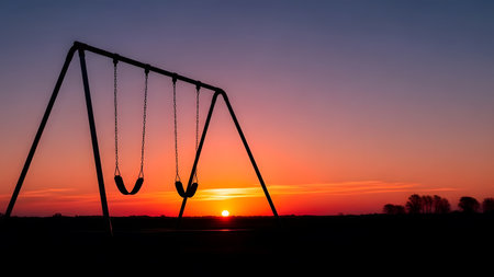 Silhouette of empty swing set. Dramatic sunset sky vibrant orange and purple hues. Horizon painted at dusk. Peaceful outdoor scene.の素材