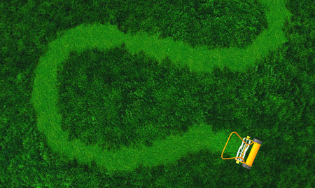 a top view of lawn where there is an orange push lawn mower in movement that is cutting the grass drawing a curved path on the grassの写真素材