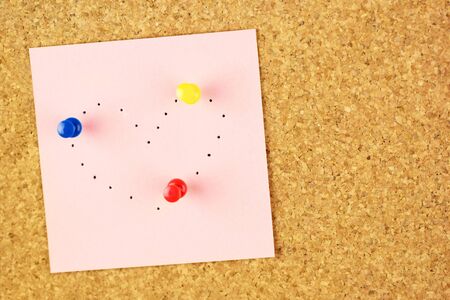 Pink sticker with heart shaped with pinholes on corkboard backgroundの写真素材