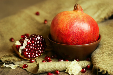 Ripe bright red pomegranate in a bowl with seeds on wooden and sacking backgroundの写真素材