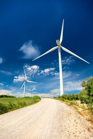 Green renewable energy concept - wind generator turbines in real landscape with grass and road, verticalの写真素材