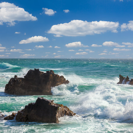 Turquoise  ocean waves slamming on the rocks of the coastline with  blue sky and white clouds at the backgroundの写真素材