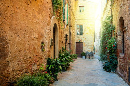 Small Old Mediterranean town - lovely Tuscan street in Pienza with sunshine and flowers, Italyのeditorial素材