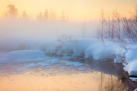 Gentle winter sunset in forest and river with beautiful misty fog, fantastic winter nature landscapeの写真素材