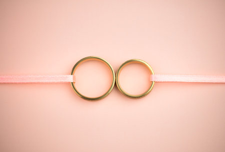 Stylish Wedding or Engagement background - pair of golden wedding rings and gentle pink ribbons and backdrop, copy space for textの写真素材