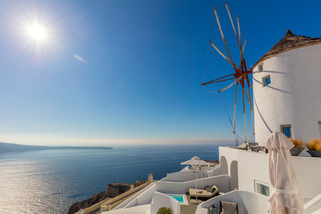 Famous windmill on Santorini island, travel in Greece. Beautiful view on white mill, sea and real sun. Small town Oia on Greek island Santorini, Europeの写真素材