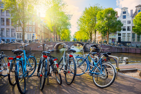 Postcard Amsterdam background - parked bicycles next to the canal, view of the traditional bridge and houses. A beautiful sunny day. Amsterdam, Holland, Netherlands, Europeの写真素材
