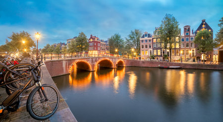 Beautiful Evening in Amsterdam. Panoramic views of the famous old houses, bicycles, bridge and canal in the old center. Illumination of the city. Amsterdam, Holland, Netherlands, Europeの写真素材