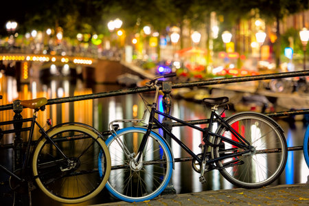 Downtown street in the evening - bike and street lights, bridge and canal with reflection in the water. Romantic night scene of Amsterdam. Netherlands, Holland, Amsterdam, Europe.の写真素材