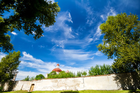 Blue sky with clouds framed by green trees old brick fence and church tower