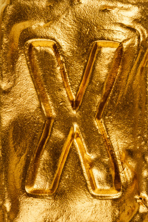 Beautiful handmade letter X on a shiny gold texture