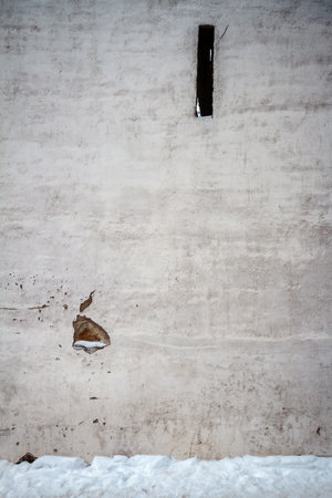 Aged weathered white plaster street wall and ground covered with snowの写真素材