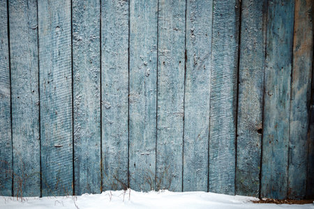 Old weathered wood plank fence and a ground covered with snow