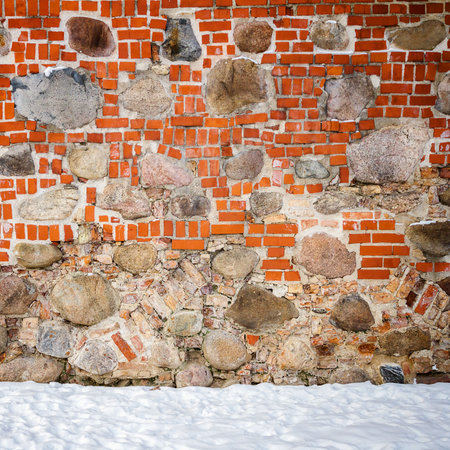 Wall of mixed materials - stone and bricks and a ground covered with snow