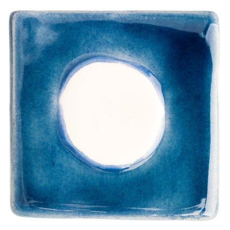 Blue handmade glazed ceramic tile with big white dot in middle isolated on whiteの写真素材
