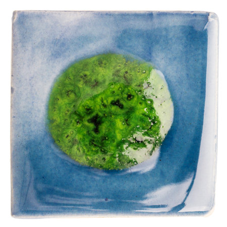 Blue handmade glazed ceramic tile with big green dot in middle isolated on whiteの写真素材