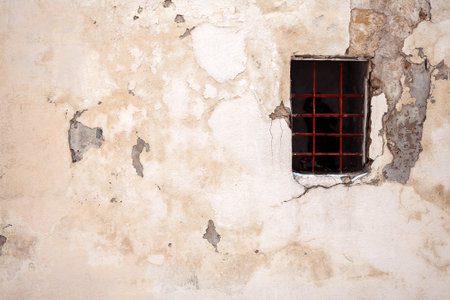 Old cracked wall with a window protected by grating