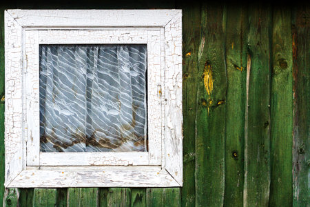 Small square window on green plank wall coversd with dirty curtain. Architecture detail backgroundの写真素材
