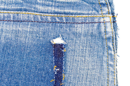 Piece of blue jeans fabric with a ripped of back pocket isolated on white background. Rough uneven...