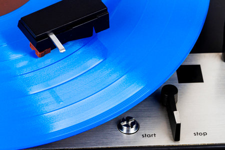 Close up of turntable cartridge on a vinyl record. Turntable playing vinyl. Needle on rotating blue...